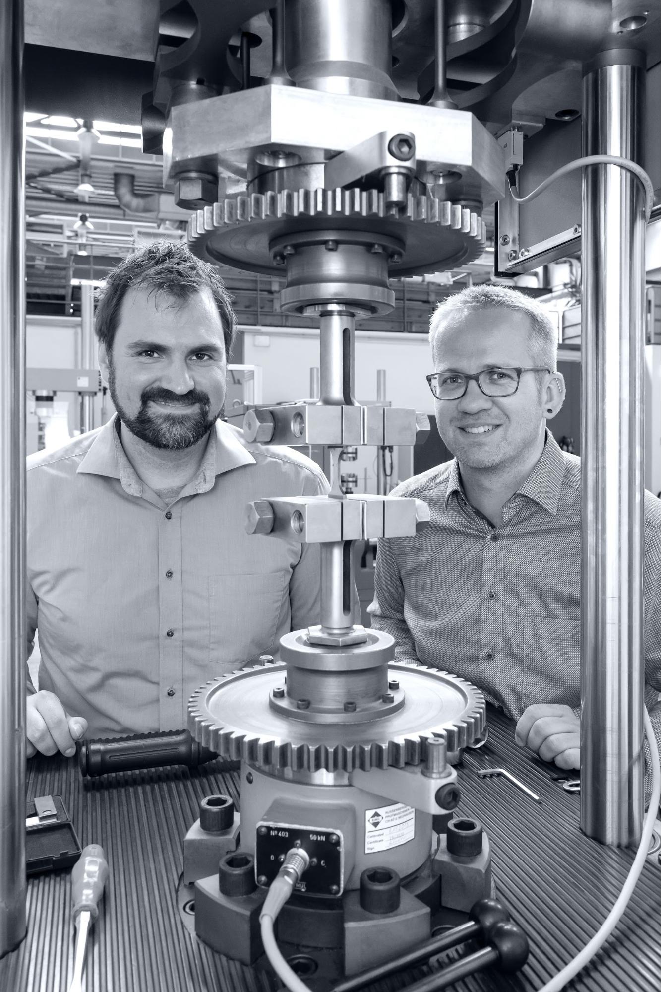 Dr. Nils Ellendt and Sebastian Huhn stand next to the fatigue testing machine